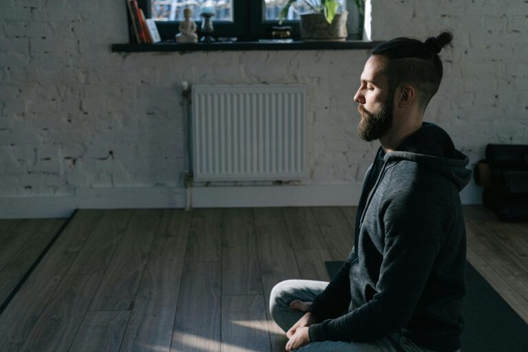 Side view of a man meditating indoors in a serene environment, promoting mental wellness and tranquility.
